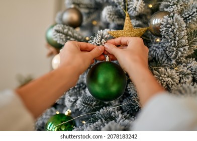 Merry Christmas and Happy New Year! Women's hands decorate a snow-covered Christmas tree with balls and toys.
