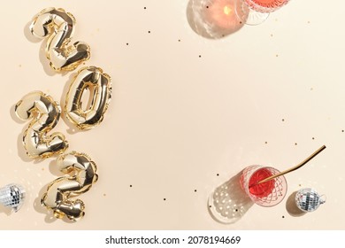 beige feestelijke achtergrond voor nieuwjaar of kerstmis met roze drankjes wijn, sap, punch, champagne en folie gouden ballonnen in de vorm van 2022