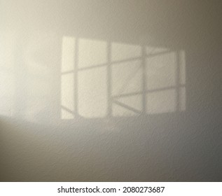 Quadrangle outlined by sunlight with straight intersecting lines inside. Shadow of window with bars is akin to famed logo. Geometric shadows on textured surface with abstract pattern.  