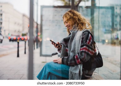 Wanita muda menggunakan ponsel pintar di stasiun bus