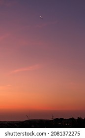 日の出で目覚めている街の美しい紫、ピンク、オレンジ色の空に上る三日月