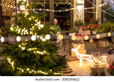Patio trasero decorado de Año Nuevo con una mujer sentada en el fondo por la noche. Mujer disfrutando de las vacaciones de invierno sola en casa