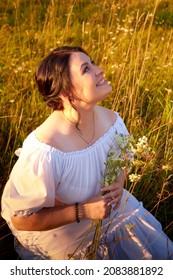Countryside plump chubby pleasant woman in white dres in green grass field. Girl in an old Russian dress of a noblewoman posing outdoors on nature in a day or a evening in Russia