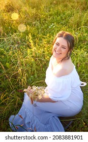 Countryside plump chubby pleasant woman in white dres in green grass field. Girl in an old Russian dress of a noblewoman posing outdoors on nature in a day or a evening in Russia