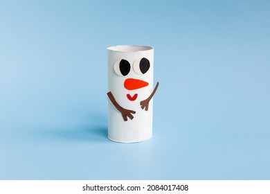 Idee ușoară de bricolaj de vacanță pentru copii. Jucărie tub rulou hârtie igienică drăguț om de zăpadă pe fundal albastru. Creativ Anul Nou și decorațiuni de Crăciun ecologic, reutilizare, reciclare concept minim realizat manual
