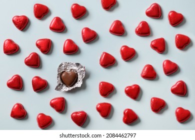 Dolci romantici al cioccolato rosso a forma di cuore in stagnola rossa e un dolce aperto su sfondo blu. Biglietto di auguri per San Valentino. Concetto d'amore.