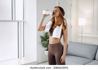 美しい女性は、非常に激しいウォームアップの後、水を飲んでいます。彼女は肩に白いタオルを持っています。彼女は右手に白い水の入ったボトルを持っています。