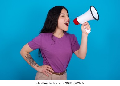 Funny Caucasian woman wearing purple T-shirt over blue background People sincere emotions lifestyle concept. Mock up copy space. Screaming in megaphone.