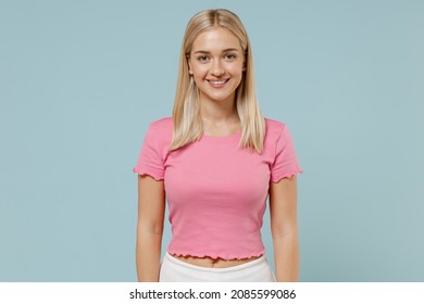 Junge, lächelnde, glückliche, fröhliche, schöne, kaukasische, blonde Frau in den Zwanzigern, die lässiges rosa T-Shirt trägt und in die Kamera schaut, isoliert auf schlichtem, hellblauem Hintergrund im Studioporträt. Menschen-Lifestyle-Konzept