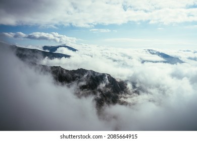 密集した低い雲の中に大きな岩と山々がある素晴らしい高山の風景。雲の上に山の頂上がある大気の高地の風景。厚い雲の上に雪の山頂が見える美しい景色。
