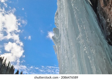 Ein riesiger gefrorener Eisblock hängt an einem Felsen, ein Winterwasserfall vor blauem Himmel in der Region Almaty.