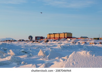 ヘリコプターは北部の沿岸集落の上空を飛行します。冬の北極の風景。氷のハンモックと雪。海岸の建物とパラボラ アンテナ。ロシアの極北、チュクチのタバイヴァーム。