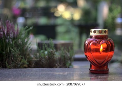 Lilin (snitch) berbentuk hati merah pada batu nisan di tanah perkuburan pada siang hari. Hari Semua Orang Suci, salin ruang.
