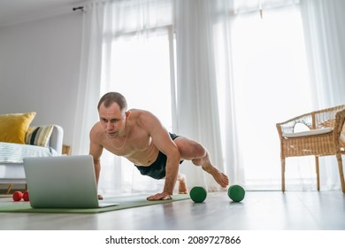 Thuis trainen in de woonkamer. Jonge gespierde lichaamsmens die spiderman push-ups maakt na online een fitnesstrainer met behulp van een laptop. Gezonde levensstijl en modern online technologieconcept.