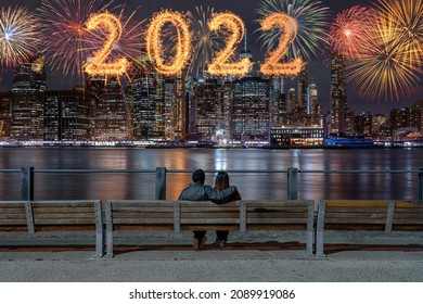 2022 ditulis dengan kembang api Sparkle dengan banyak warna kembang api di sisi belakang pasangan duduk dan melihat latar belakang Cityscape New york, cakrawala pusat kota AS, Selamat tahun baru dan selamat konsep Natal