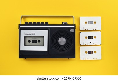 Antiquated retro-style portable stereo radio with cassette recorder and audio cassettes from around the late 70s on a yellow background. Music listening concept. Vintage. 