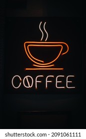 Bright orange neon sign with a picture of a coffee cup and text coffee on a dark background