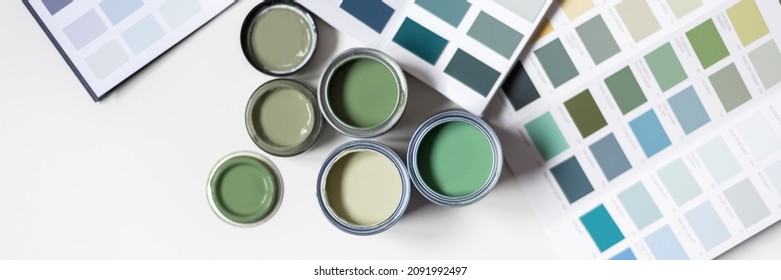 Winzige Musterfarbdosen während der Hausrenovierung, Prozess der Farbauswahl für die Wände, verschiedene grüne Farben, Farbkarten auf dem Hintergrund, Bannergröße