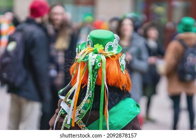 Tampilan belakang gadis berambut merah bertopi dengan dekorasi, simbol Hari St. Patrick, parade di kota