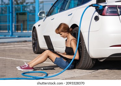 Cô gái đang đợi trên mặt đất trong khi xe điện của cô đang sạc. Đang làm việc trên máy tính xách tay.