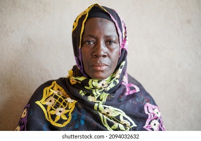 Cận cảnh chân dung người phụ nữ châu Phi nhìn thẳng vào máy ảnh bên bức tường trong ngôi làng ở Mali