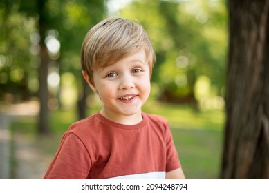 Joyful little boy. He is smiling on the background of a green park. The boy looks into the camera lens
