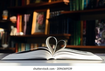 Background - bookshelves lit by the sun. An open book is on the table. Pages are folded in the shape of a heart.  Concept - Valentine's Day