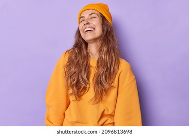 鼻にピアスをした屈託のない楽観的な女性は笑い、喜んで目を閉じたままにします。白い歯は、紫色の背景に隔離されたカジュアルな服を着て、ポジティブな感情を表現しています。