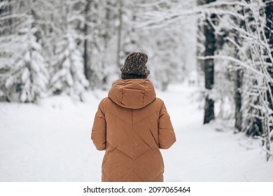 Mujer con chaqueta cálida de invierno caminando en un bosque de pinos de invierno cubierto de nieve. Vista desde atrás.