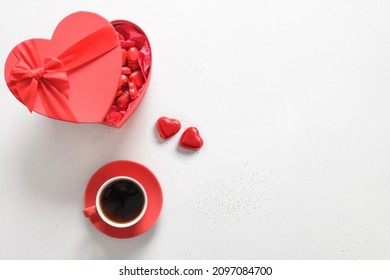 Cawan kopi hitam, gula-gula coklat merah sebagai hati dalam kotak pada latar belakang putih. Kad ucapan hari Valentine. Tarikh romantik. Pemandangan dari atas. Salin ruang.