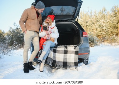pareja, chico y chica sentados en un auto jugando con un perro en el bosque invernal