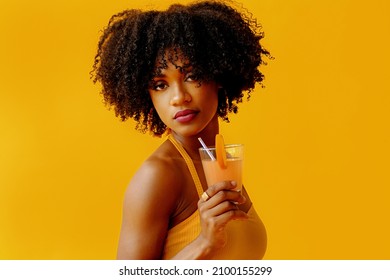 beautiful young African american woman in bright summer outfit drinking refreshing cocktail isolated on yellow background