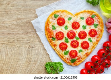 Heart shaped Italian margherita pizza with tomatoes,mozzarella cheeses and parsley on parchment paper with wooden background.Love vegetarian food concept for Valentine's day.Top view.copy space