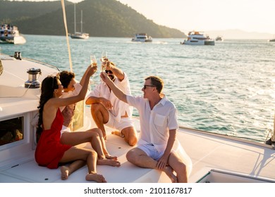 Un grupo de amigos, hombres y mujeres, disfrutan de la fiesta bebiendo champán mientras hablan juntos mientras navegan en catamarán al atardecer de verano. Hombres y mujeres relajan el estilo de vida al aire libre en vacaciones tropicales