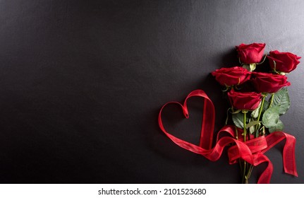 Concepto de amor y día de San Valentín hecho de rosa roja y cinta de corazón sobre fondo de madera negra. Vista superior con espacio de copia, plano.