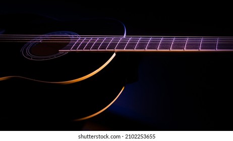 コピー スペースと色付きの光のビームの下で暗い背景に黒のギター。ギター音楽の控えめなコンセプト