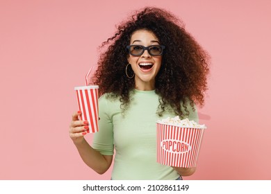 Leuke opgewonden vrolijke jonge krullende Latijns-vrouw 20s draagt ​​mint t-shirt in 3D-bril kijken naar film film houden emmer popcorn kopje frisdrank geïsoleerd op effen pastel licht roze achtergrond studio portret