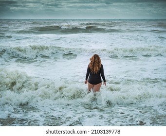 Weibliche Schwimmerin mit langen Haaren, die einen Neoprenanzug tragen, der in raue See geht