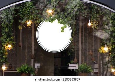 デザイン用の空白の最小限の円形ショップ看板モックアップ。葉に光の花輪を添えたロゴプレゼンテーション用の街路吊り看板。メタル カフェ レストランまたはバー バッジ ブラック ホワイト ラウンド。