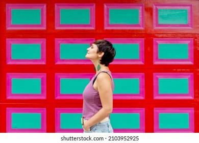Vista lateral recortada de una mujer parada contra una pared a cuadros decorada con rectángulos rojos y verdes. Vista horizontal de una mujer latinoamericana aislada sobre una pared colorida con ropa de verano.