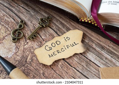 God is Merciful, handwritten Bible quote with an old, vintage key and treble clef on a wooden table. Christian biblical concept of Jesus Christ's grace and love. A closeup.