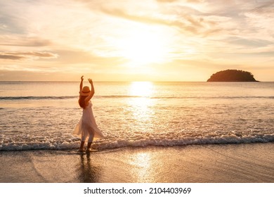 Young woman traveler dancing and enjoying beautiful Sunset on the tranquil beach, Travel on summer vacation concept