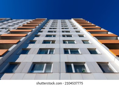 Hoog flatgebouw uit de 20e eeuw met 11 verdiepingen en oranje balkonboringen vanuit kikkerperspectief met uitlijnlijnen. Ramen en gevel op een zonnige dag met blauwe lucht.