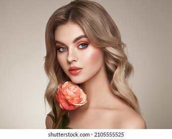 A beautiful young woman with shiny wavy blonde hair. Model with healthy skin, close up portrait. Girl with a rose flower