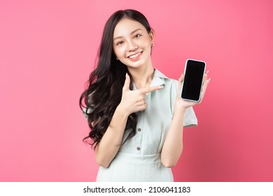 Young Asian woman holding phone in hand and pointing at it with playful expression	