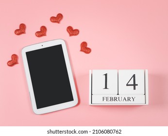Vista superior o disposición plana del calendario de madera 14 de febrero, tableta digital de pantalla en blanco para espacio de copia y corazones de brillo rojo sobre fondo rosa. Día de San Valentín y mensaje de amor en las redes sociales.