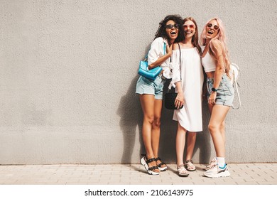トレンディな夏服を着た 3 人の若い美しい笑顔の女性。セクシーな屈託のない多民族の女性が壁の近くの通りの背景にポーズします。サングラスで楽しんでいる肯定的なモデル。陽気で幸せ