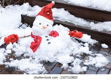 Ongelukkige sneeuwman in wanten, rode sjaal en muts smelt buiten in het zonlicht op nat trottoir. De lente nadert, warme winter, klimaatveranderingconcept