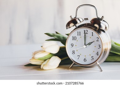 Konzept der Sommerzeit. Stellen Sie Ihre Uhren und auf 2 Uhr morgens mit diesem Bild eines Weckers mit weißen Tulpen-Blumen ein. Selektiver Fokus mit unscharfem Vordergrund und Hintergrund mit Kopierraum.