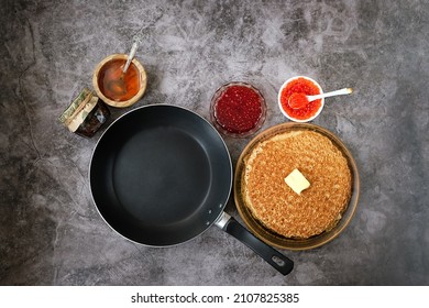 pancakes on plate, red caviar, jam, honey, frying pan on dark table background. Maslenitsa holiday, pancakes week. traditional slavic festival meal. flat lay
